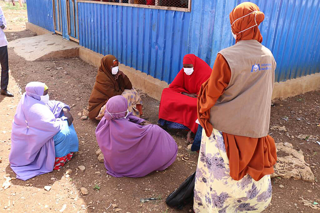 Rowly Humow (standing) shares information about how to prevent COVID-19, and what the signs and symptoms of the virus are, with women at Banow IDP camp.