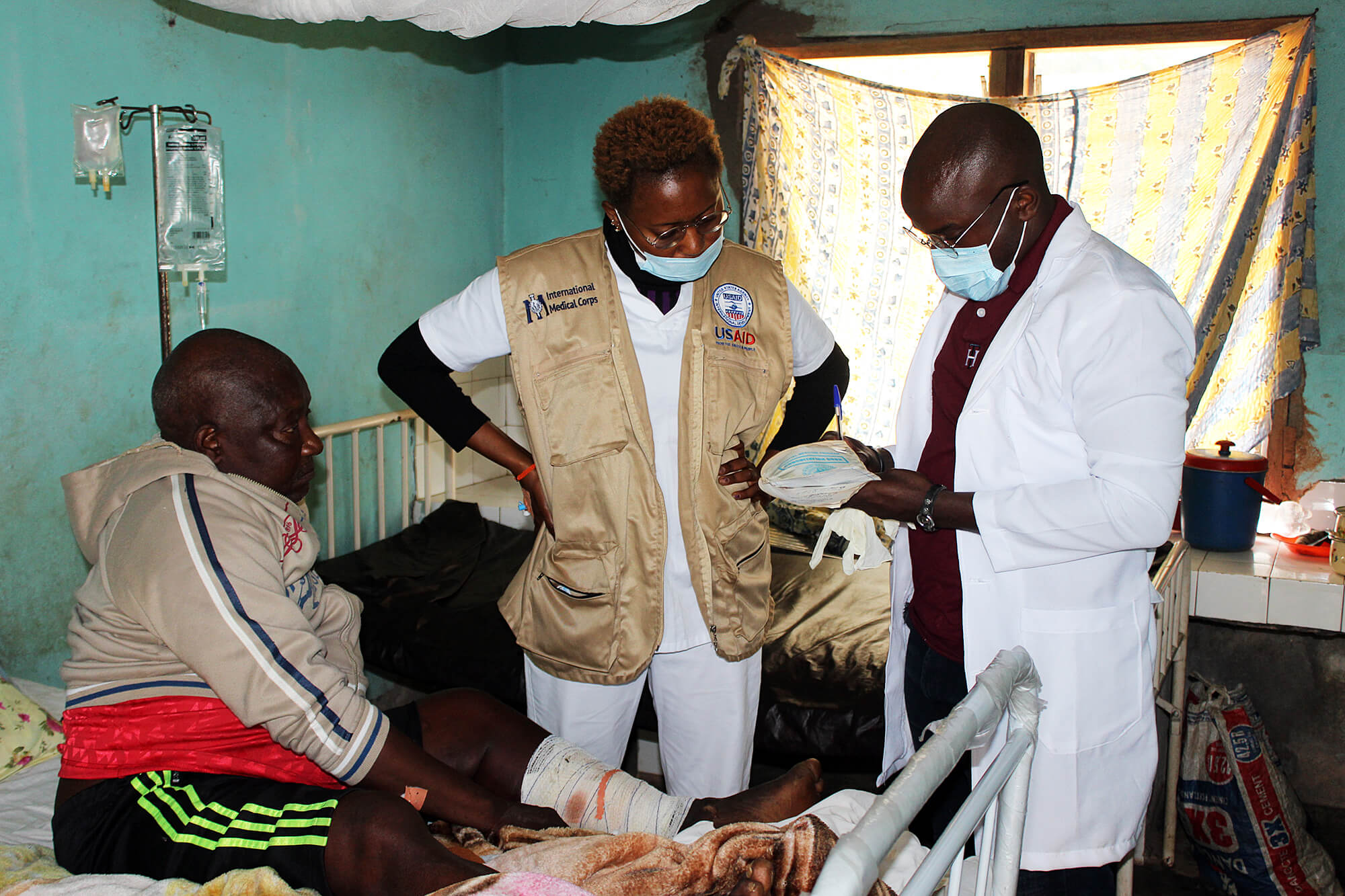 Dr. Norbert Lemonge, a general practitioner and Health Activities Project Manager, and Nurse Judit Manyong check on a patient with a gunshot wound during ward rounds in Konda IHC. In this region, a war is causing injury and death among civilians.