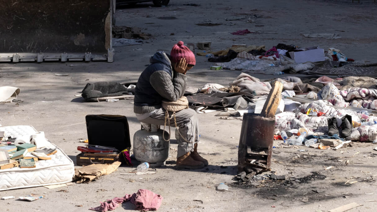 A young woman who survived the earthquakes sits next to rubble in Hatay, Turkey. 