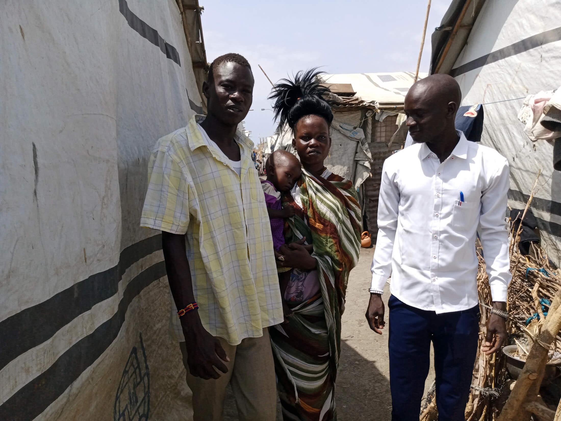 Phillip (left) stands with his wife, child and Duku Evans Chaplain in the Malakal PoC site.