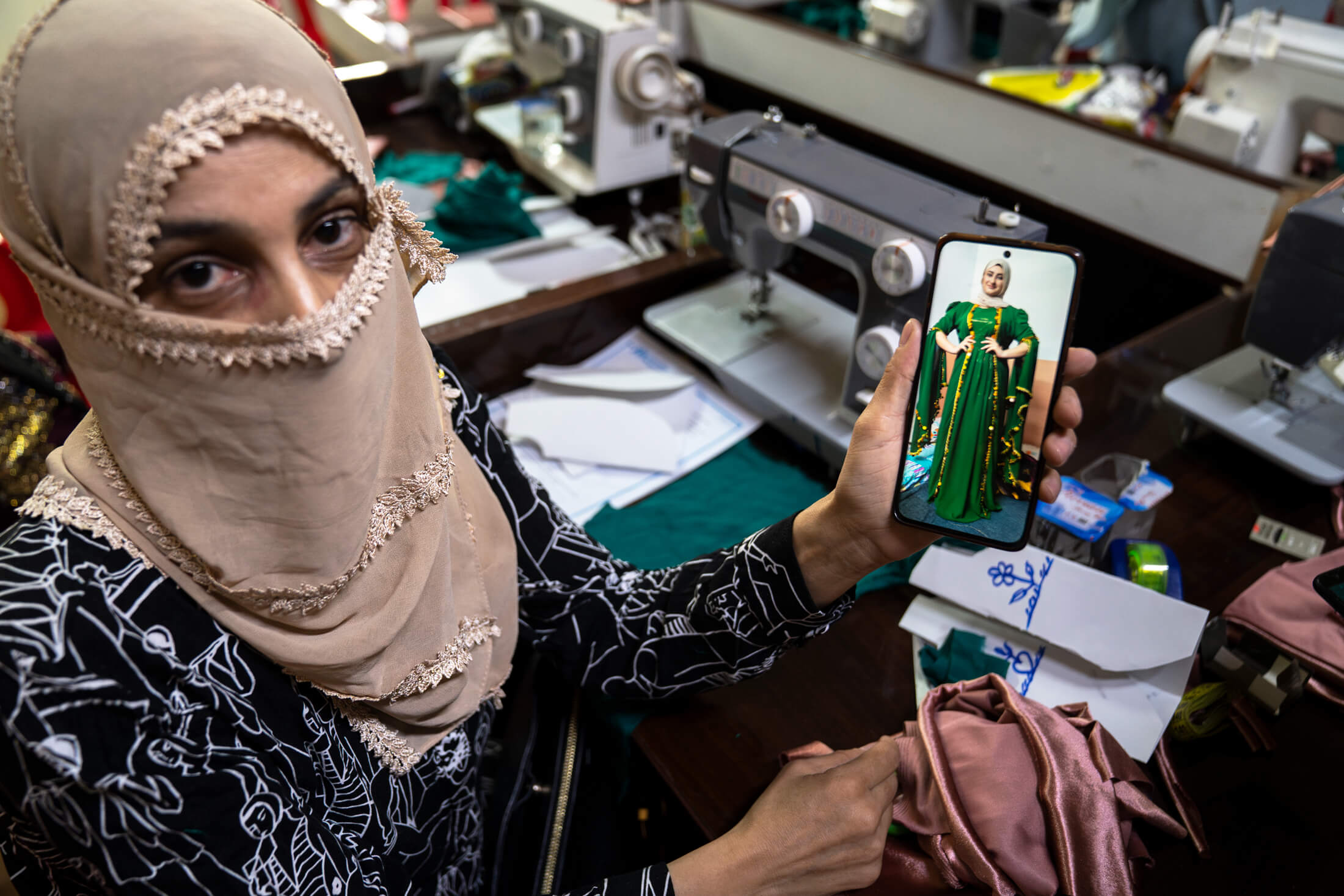 Seated at her sewing machine station, Atya, 38, shows a photo of a dress she made using the skills she learned during the tailoring vocational training. Originally from Hasakah, Syria, she and her mother were forced to flee the violence in 2018. She has lived in Domiz 1 refugee camp ever since.