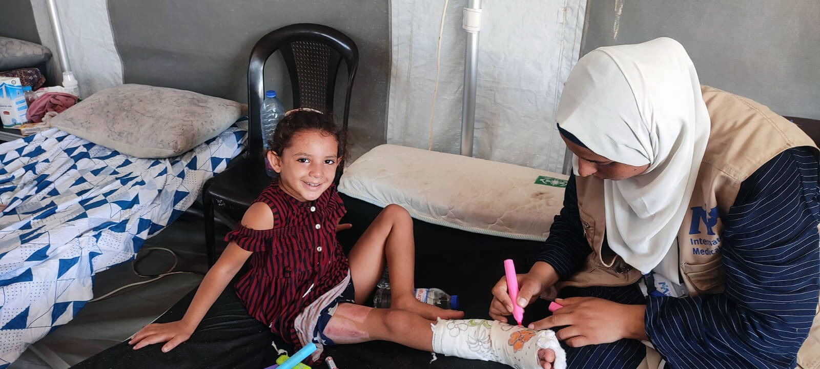 A staff member draws on Ghazal’s cast in the hospital tent.