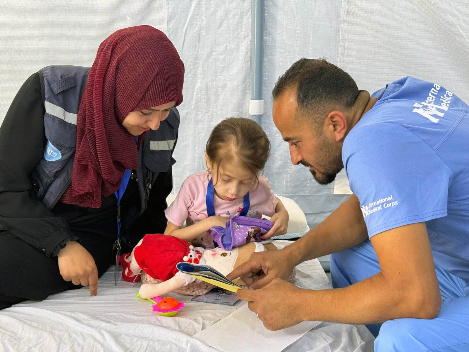 Nutrition Supervisor Dr. Mariam Ibrahim Al-Bayyouk and Pediatrician Dr. Mohammed Fayeq Abed play with Jana at the International Medical Corps field hospital in Deir Al Balah, Gaza.