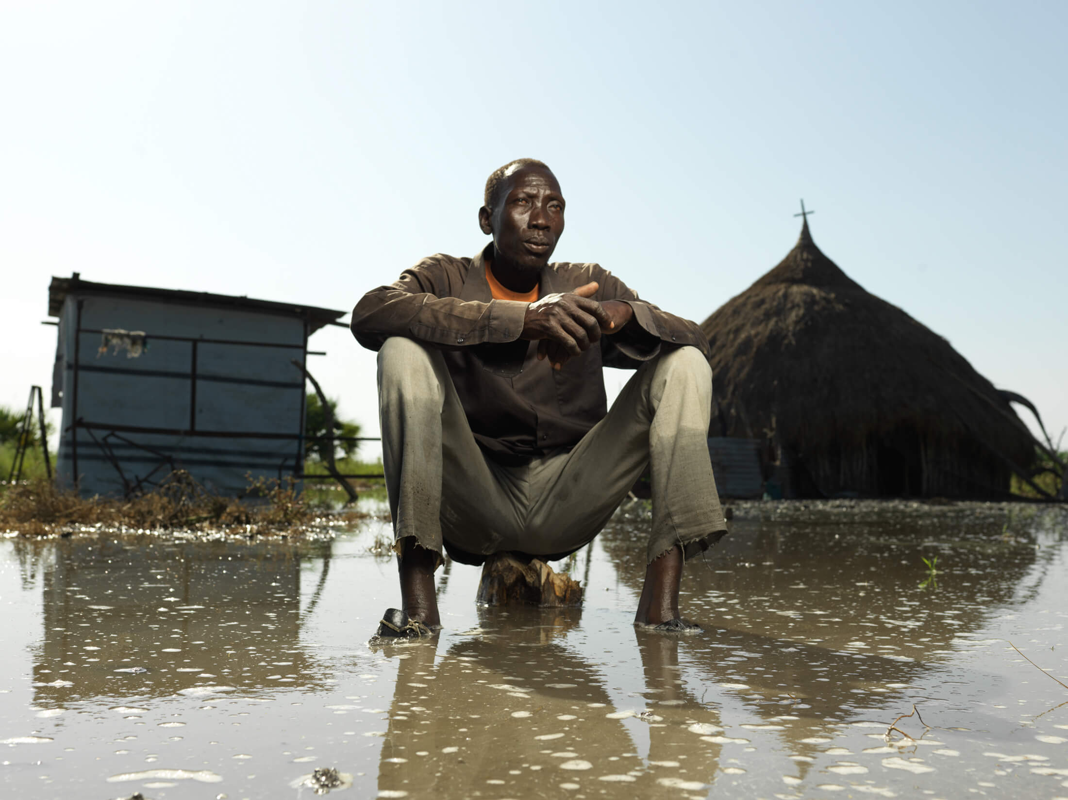 Mabek Chol sits in front of the flooded home that he was forced to abandon.