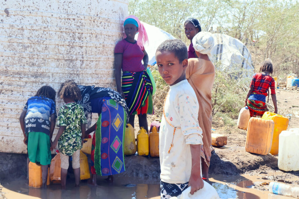 Women and children displaced by the earthquakes gather water to take back to their families.