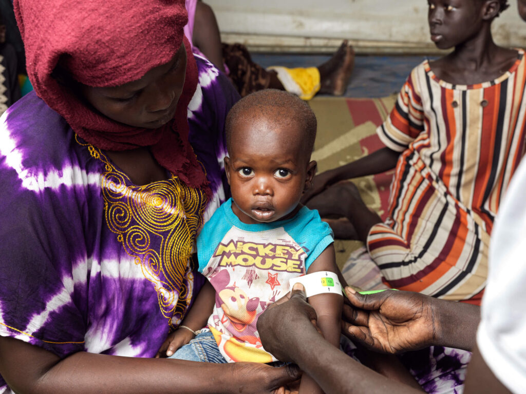 An International Medical Corps health worker in South Sudan screens 18-month-old Pal Tut for malnutrition using a mid-upper arm circumference measuring tape.