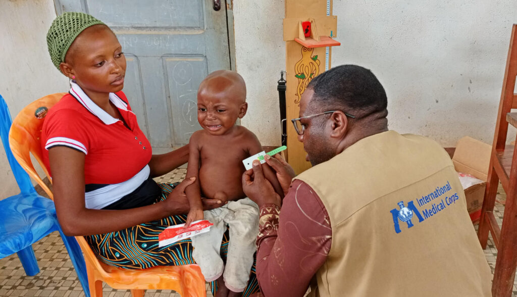 An International Medical Corps nutrition assistant shows Chodelia how to measure her son’s mid-upper arm to screen for malnutrition.