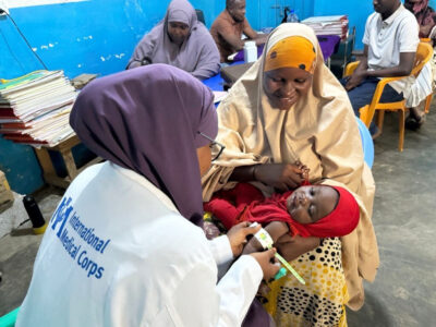 An International Medical Corps health worker takes Kifaayo’s MUAC measurement while she sits in her mother’s lap.