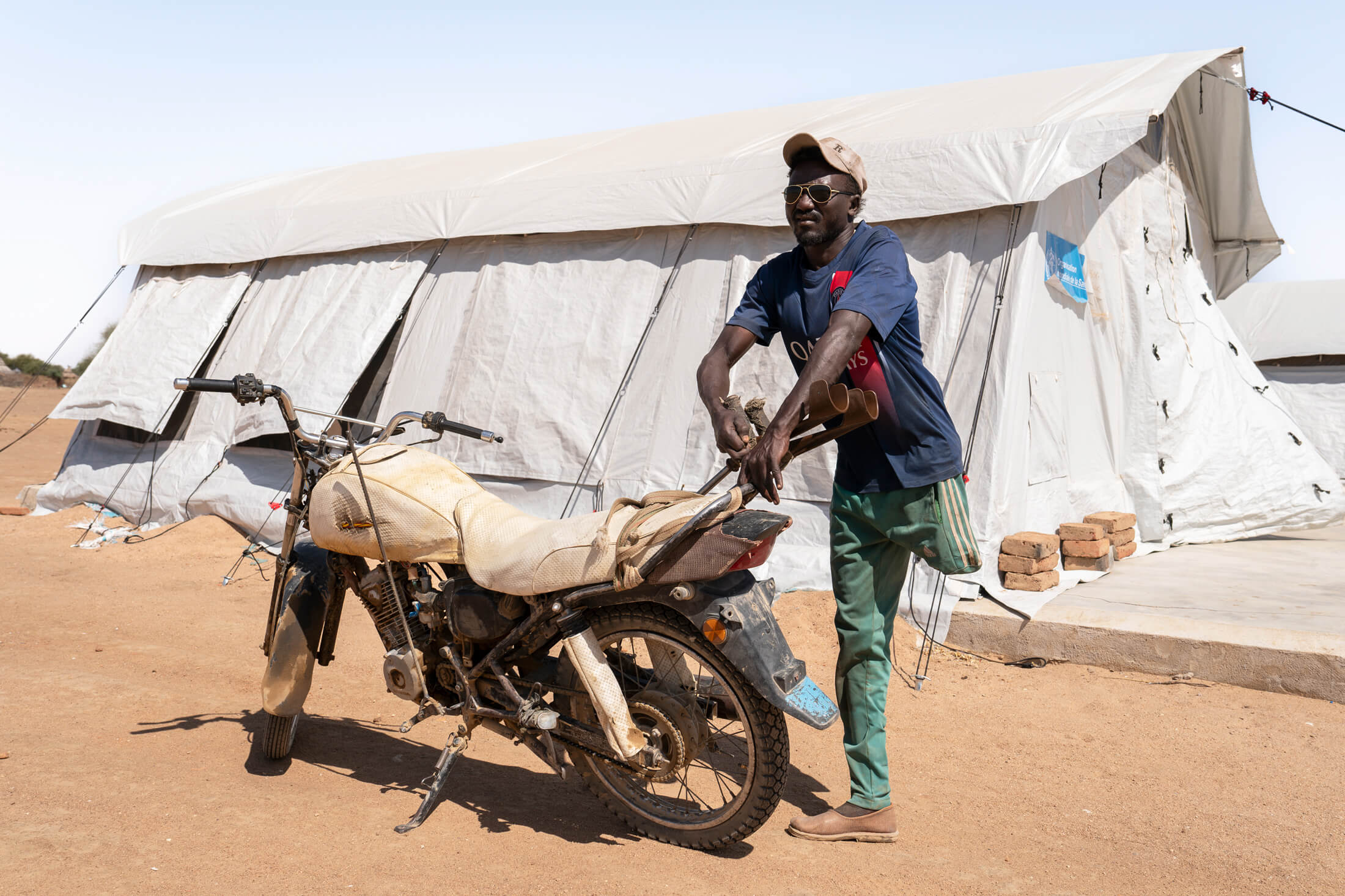 Aziber rests against his motorcycle, surveying his temporary home in Dougui, Chad.