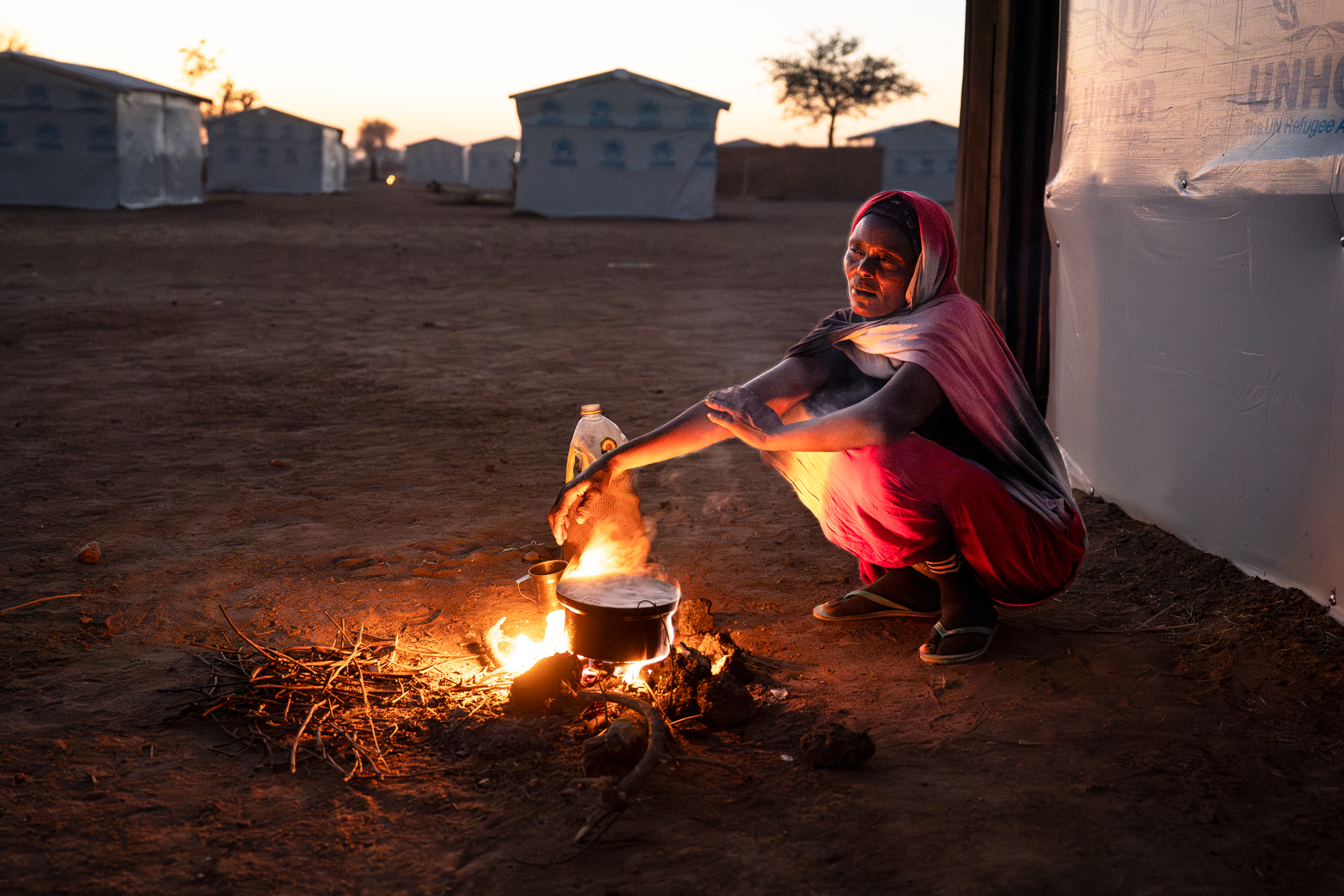 A woman cooks dinner outside her new shelter in Dougui refugee camp.