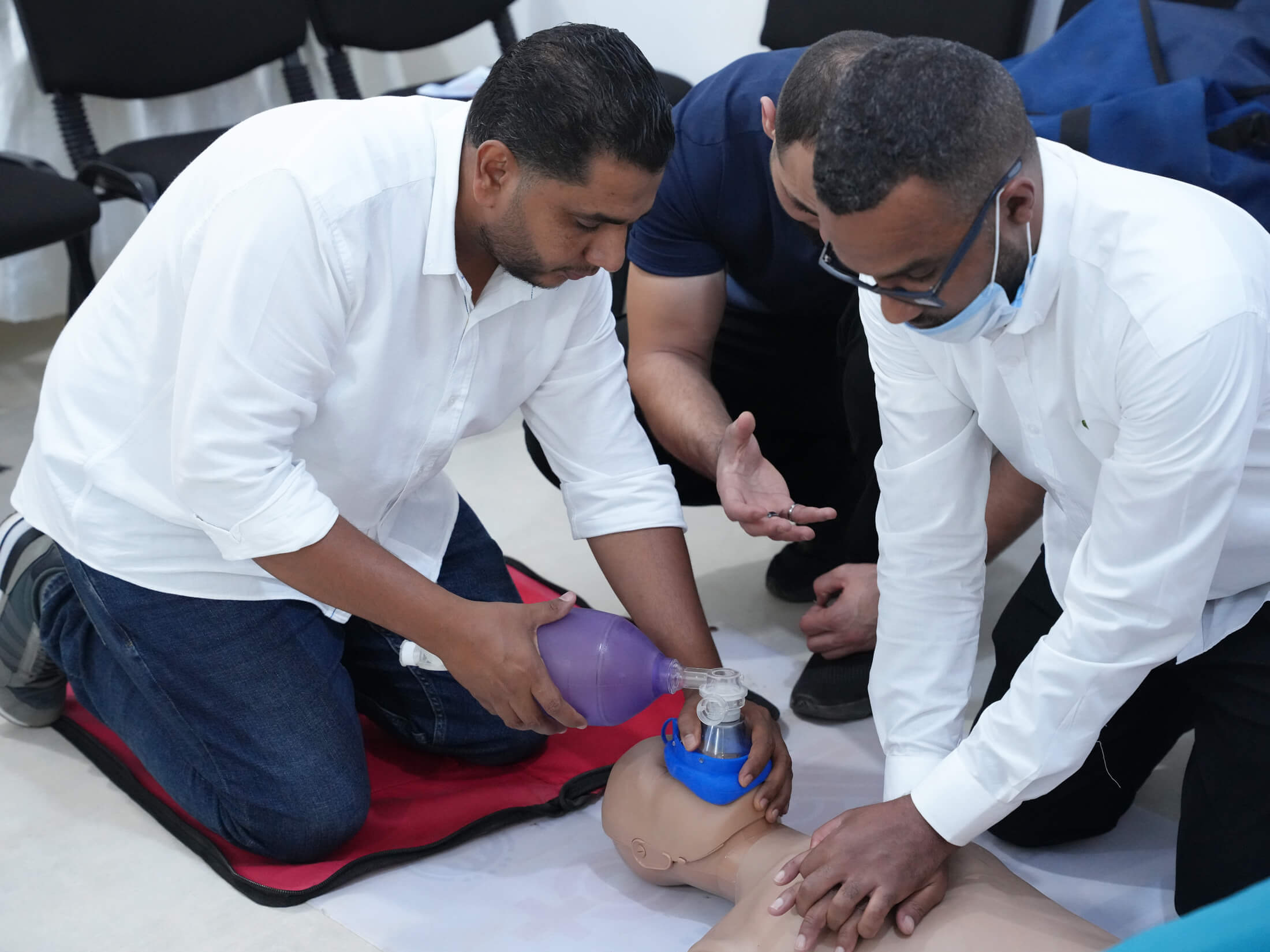 Dr. Jalal Nasouf (left) and Dr. Bashier Mohamed (right) practice CPR during a basic life support training session, with Dr. Ahmed Fauzi, LEMA staff member (middle), providing guidance.