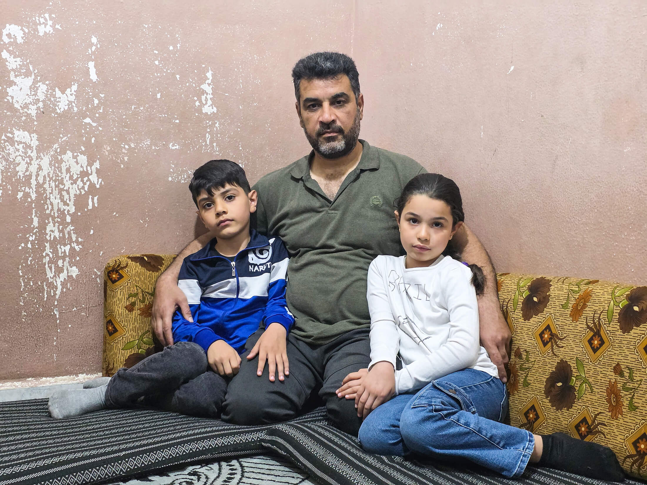 Mounir, a Syrian refugee, sits with his youngest kids, Maha (right) and Jihad (left), who underwent surgery to repair their umbilical hernias, thanks to free and comprehensive medical support provided by International Medical Corps.