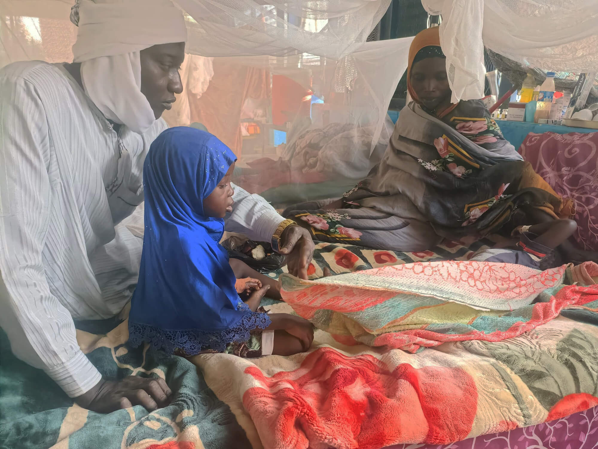 Hassan (left) and his family sit together in Umdukhun Hospital, where his young son received treatment for measles.