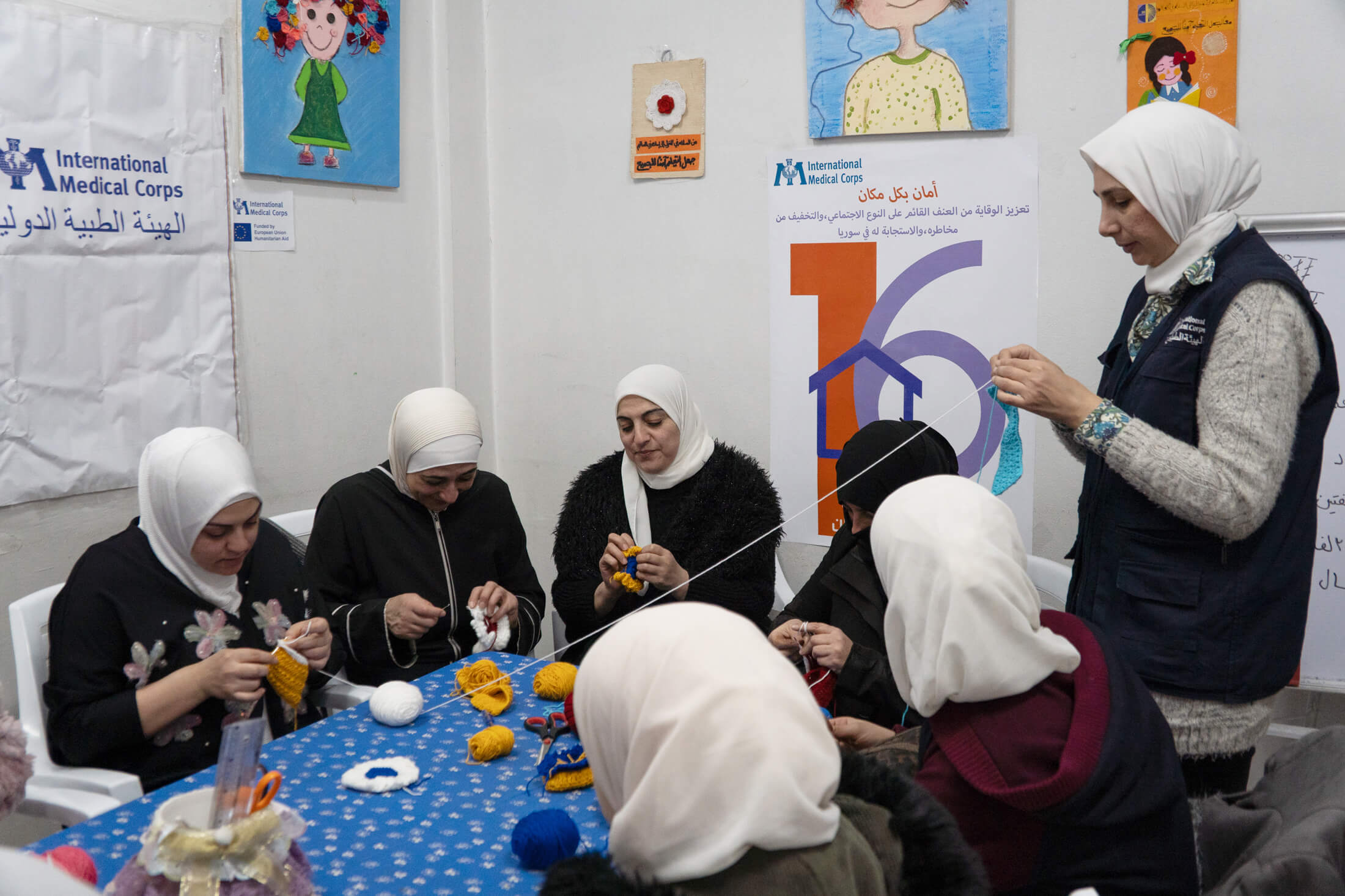 A group of women and girls participate in a crochet session with Reem AlKhalidi (standing).
