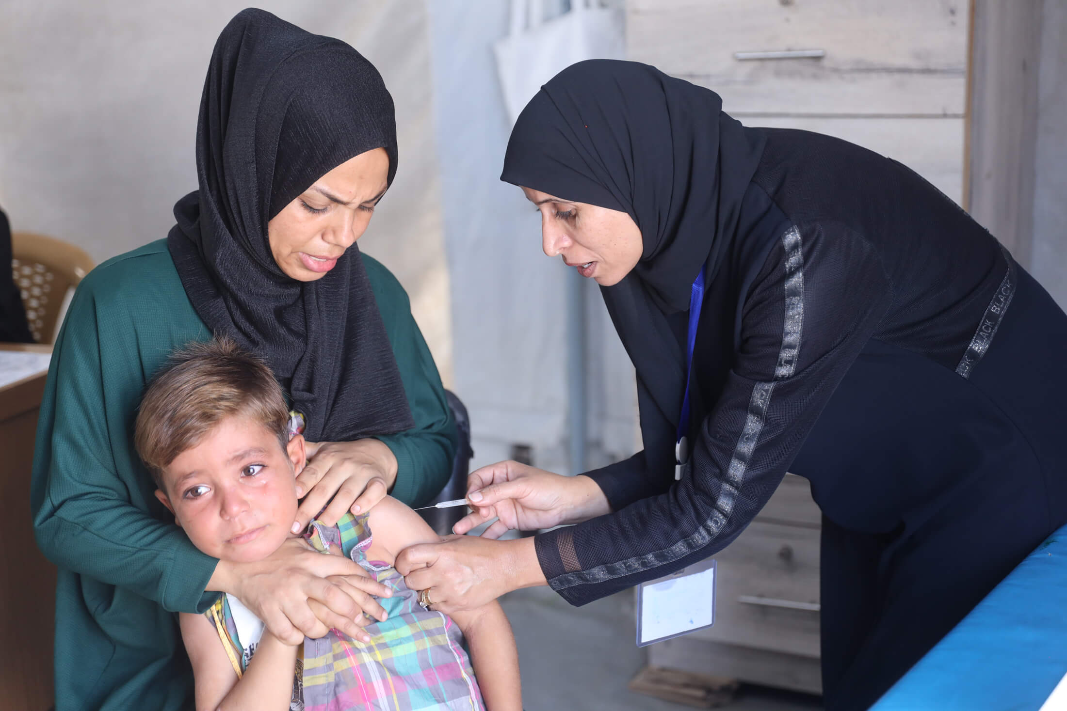 An International Medical Corps nurse (right) vaccinates a child as his caregiver comforts him.