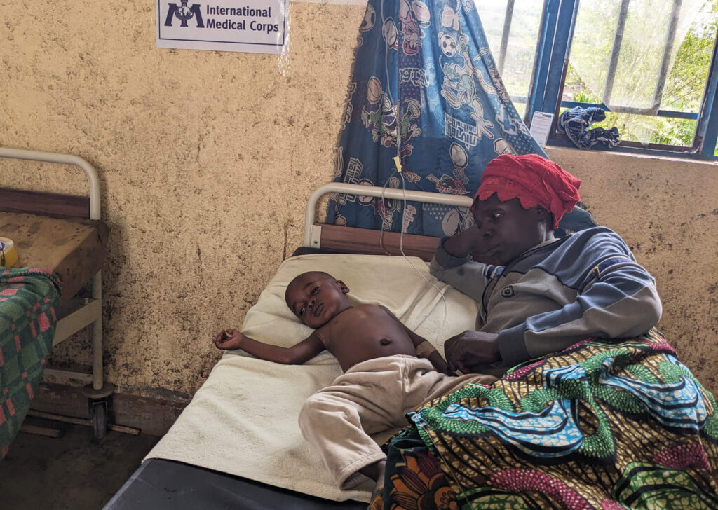 Justine lies beside Ombeni during his treatment at International Medical Corps’ MMU.