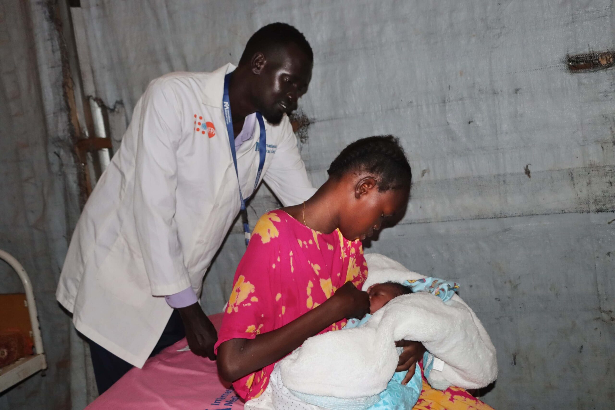 Senior Midwife Supervisor Chuol Ker Yat Pan stands with patient Nyachuom-Domach and her newborn baby in Juba IDP Camp.